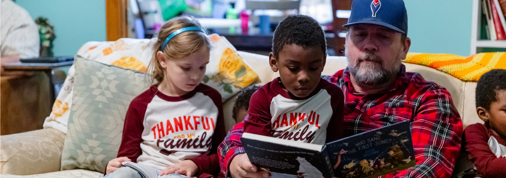 An adoptive dad reads a book with his children on the couch.